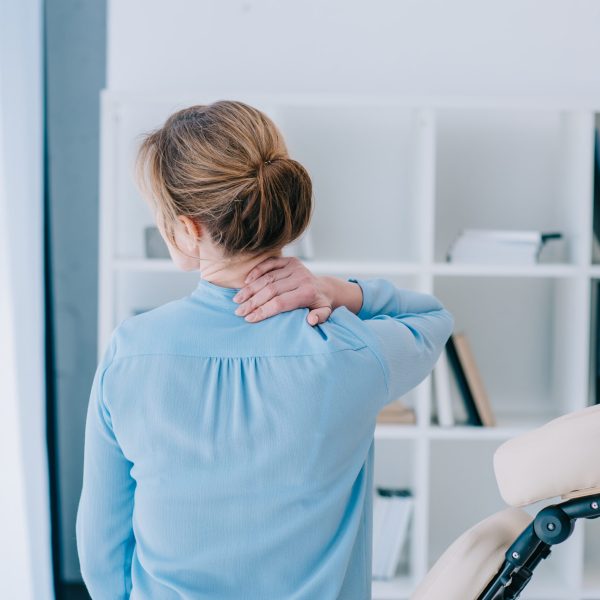 rear view of businesswoman with neckpain sitting on massage chair